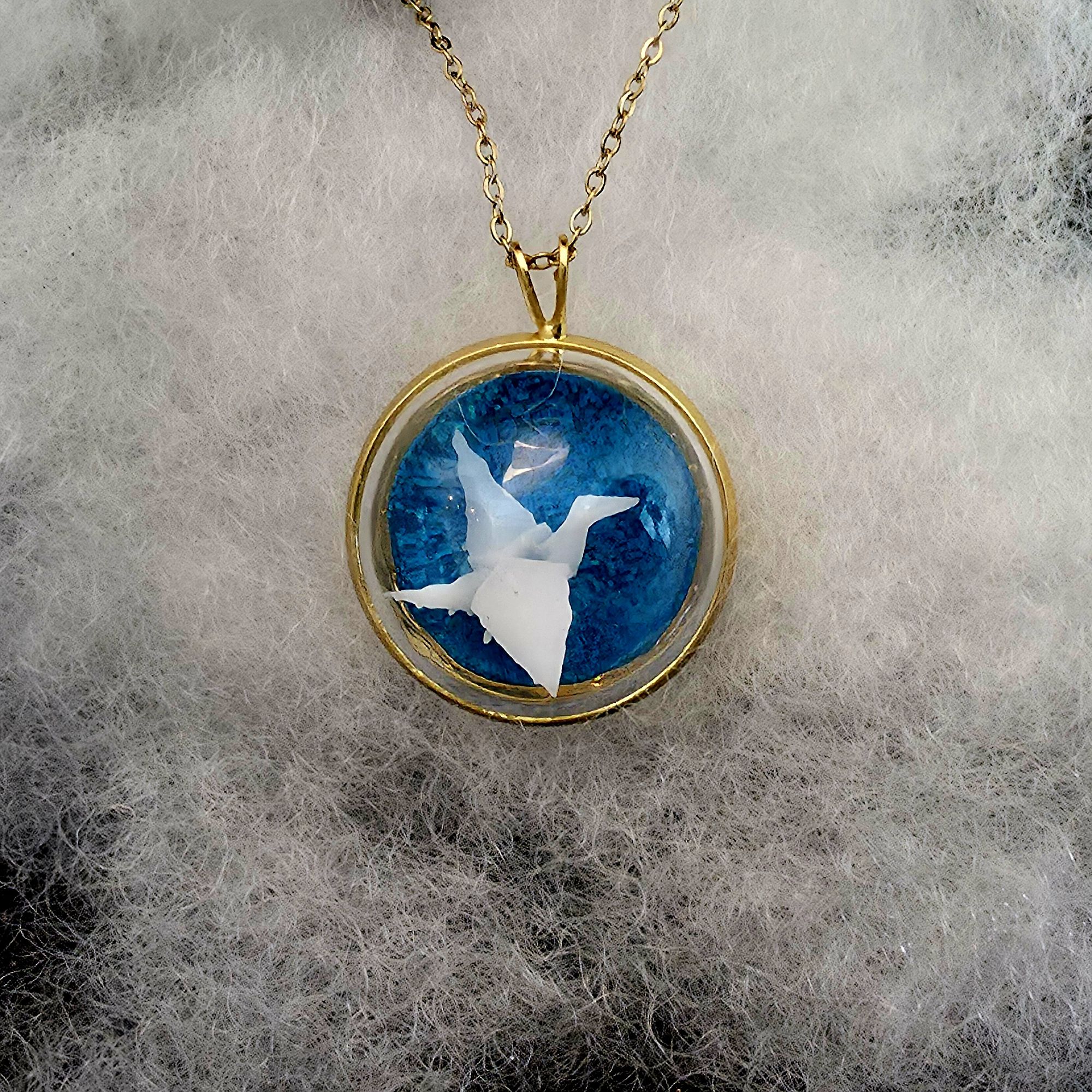 médaillon en métal doré contenant un oiseau origami blanc sous une bulle de verre - petite planete