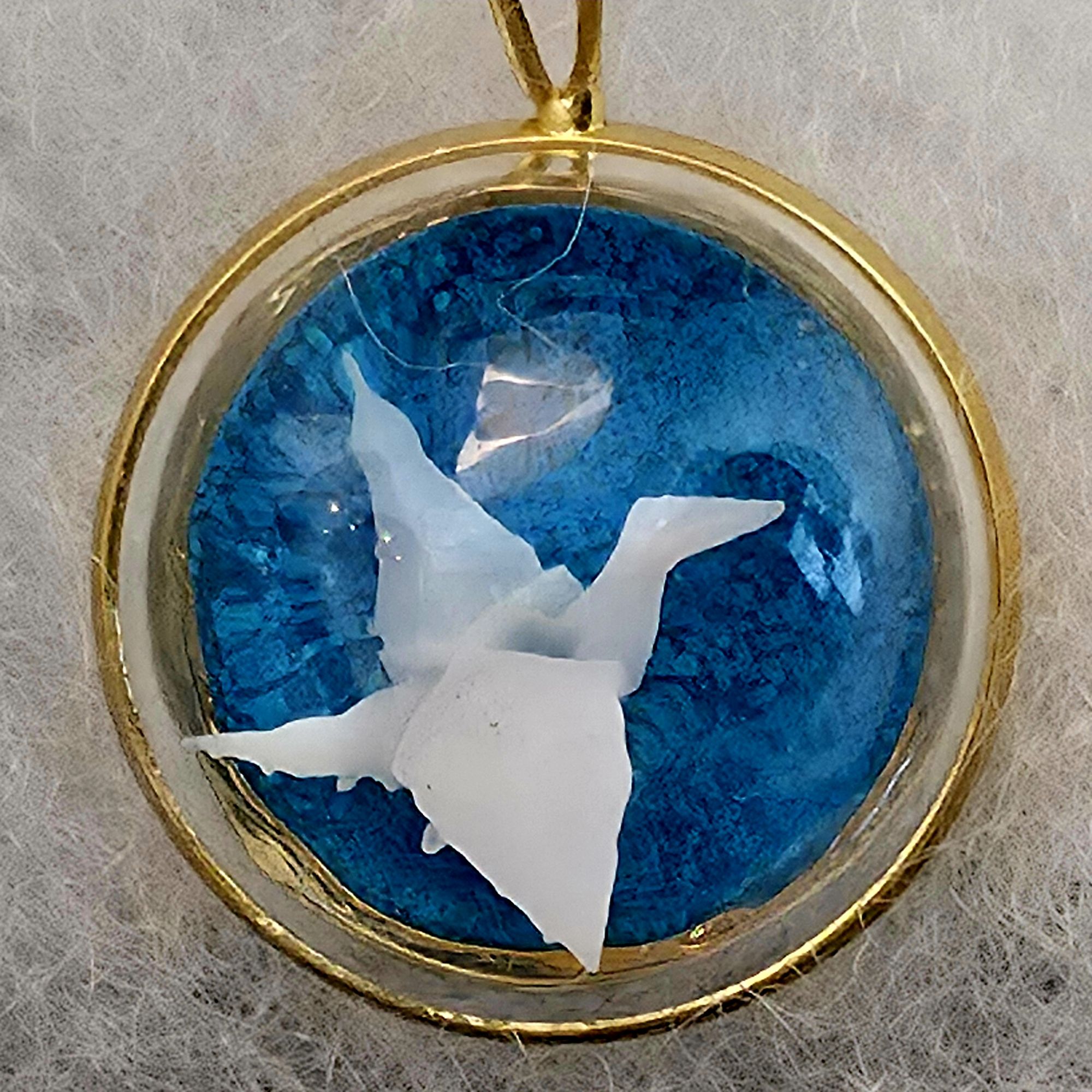 médaillon en métal doré contenant un oiseau origami blanc fond bleu sous bulle de verre - petite planete