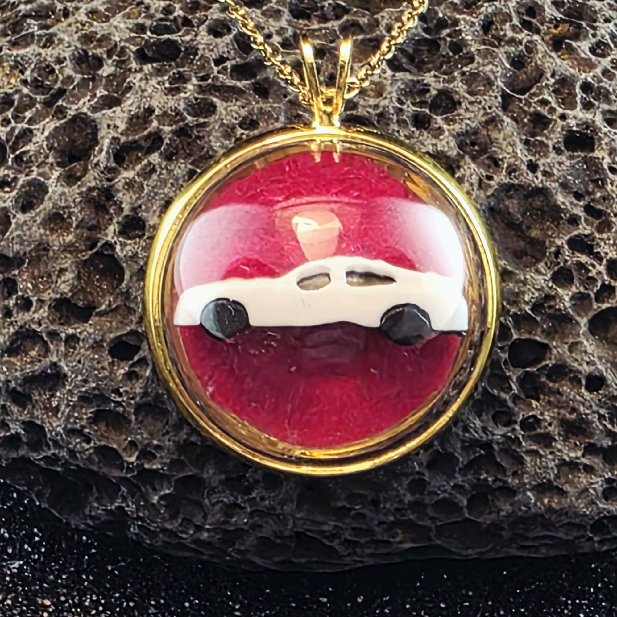 médaillon en métal doré contenant une voiture blanche sur fond fuschia sous bulle de verre - petite planete