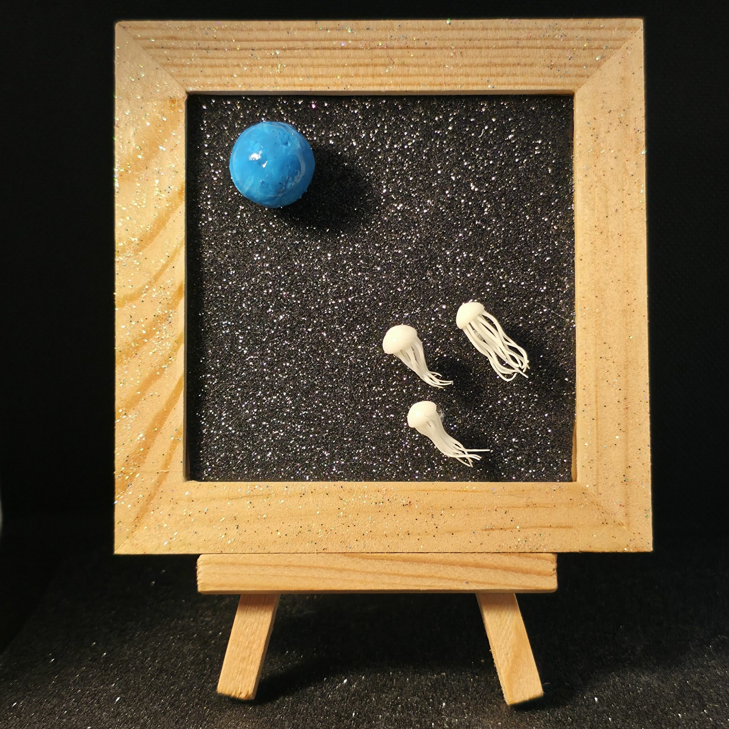 Tableau en bois présentant des méduses de l'espace se dirigeant vers la terre, devenue totalement bleue suite à la hausse du niveau des océans