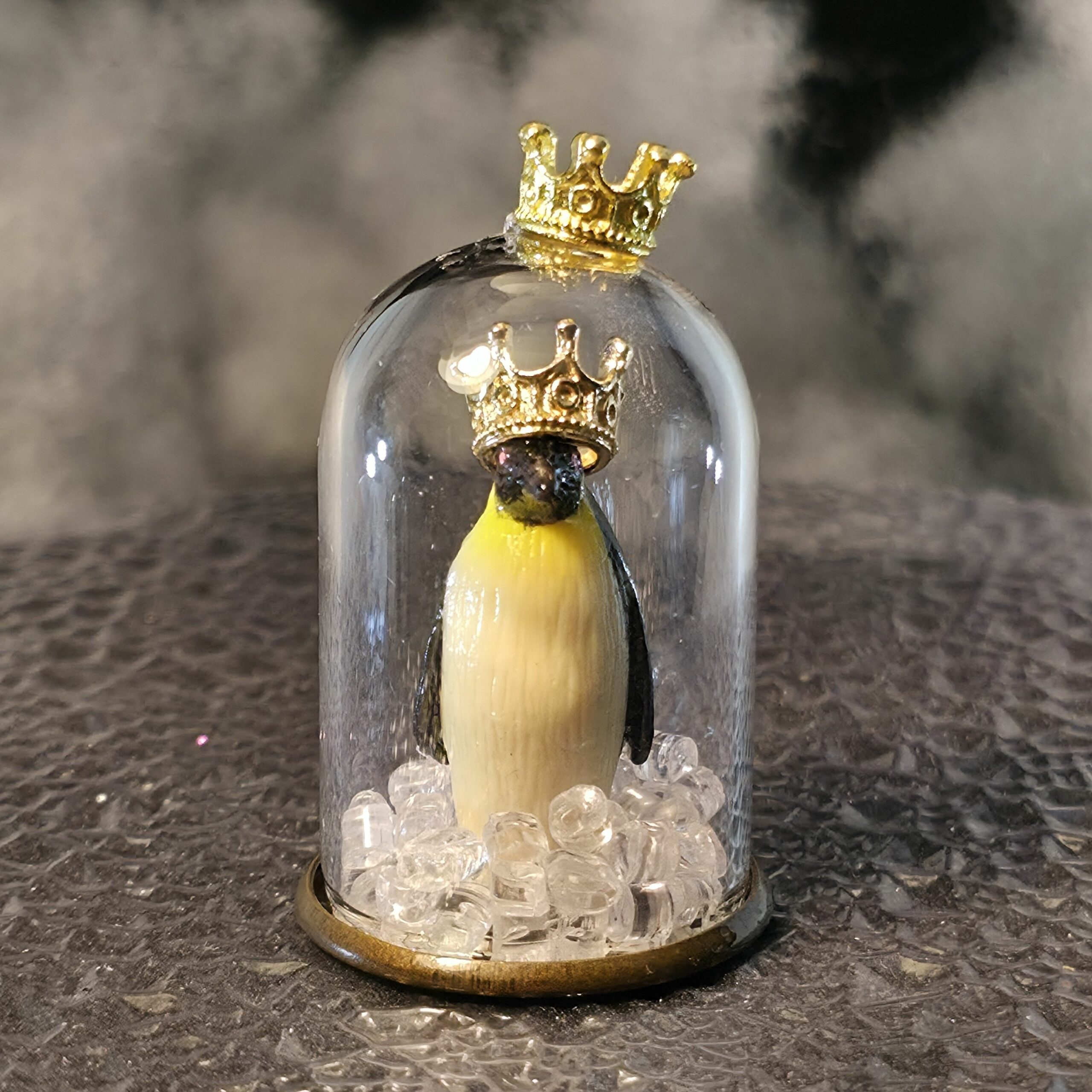 bulle de verre avec couronne contenant une figurine de pingouin/manchot empereur debout coiffé lui-aussi d'une couronne, entouré de glaçons pour l'éternité - petite planete