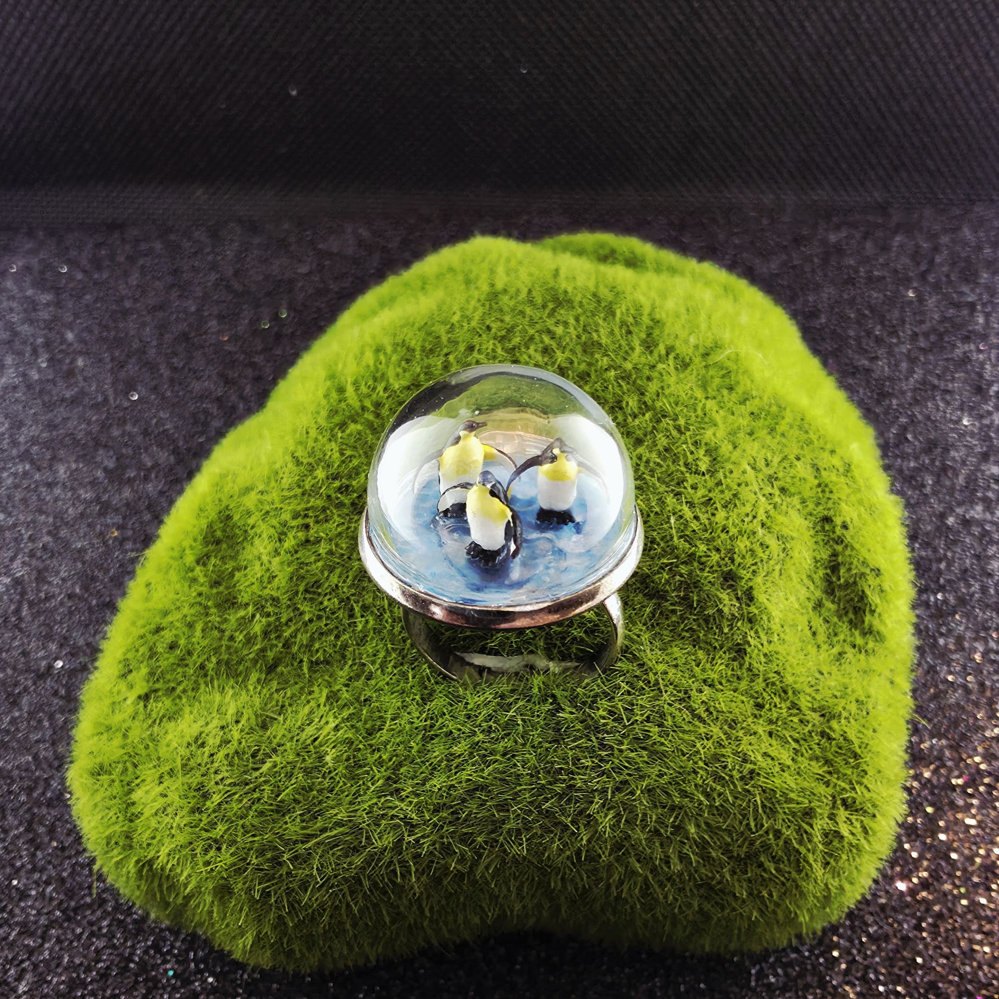 Bague en métal et bulle de verre présentant trois mini pingouins sur la glace