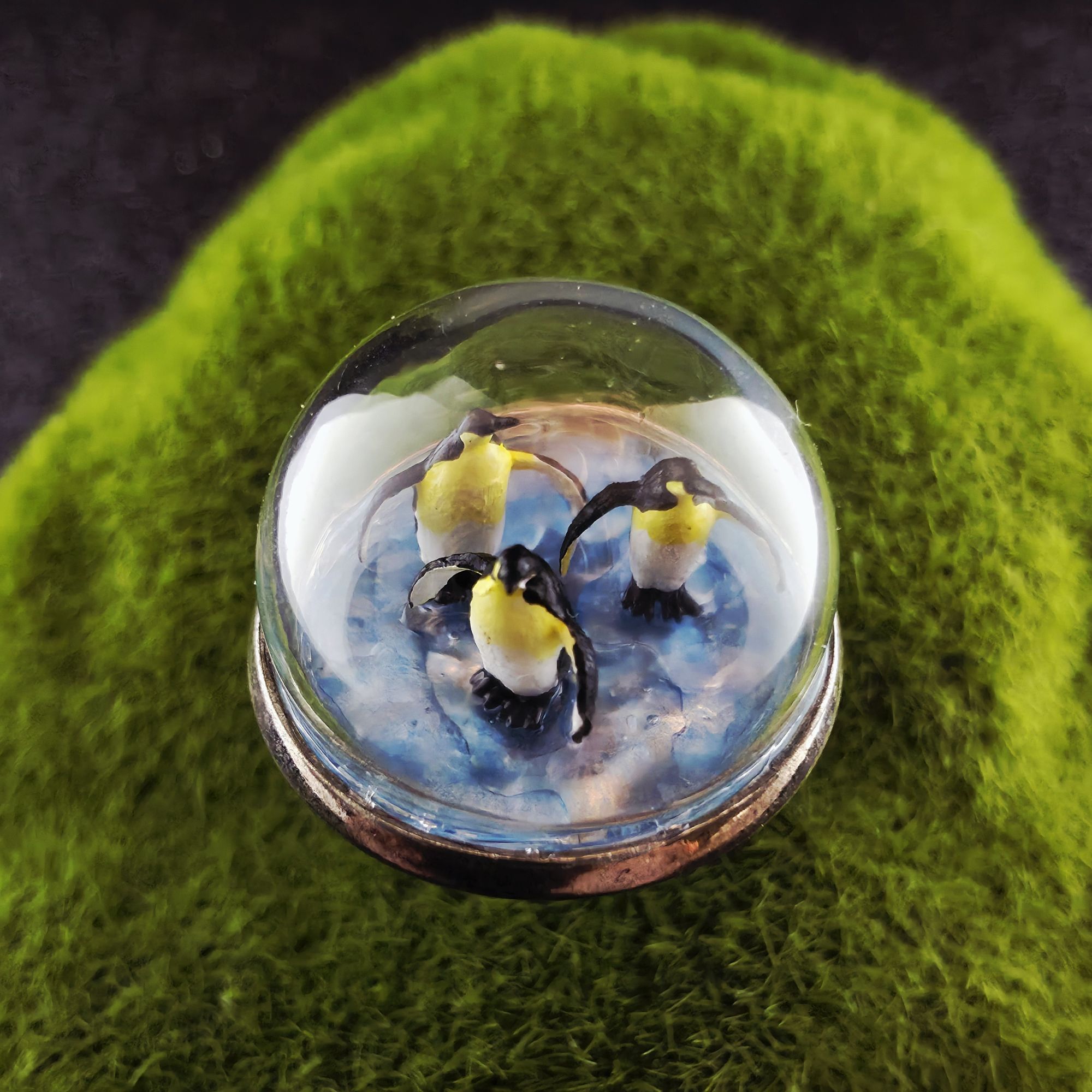 Bague en métal et bulle de verre présentant trois mini pingouins sur la glace