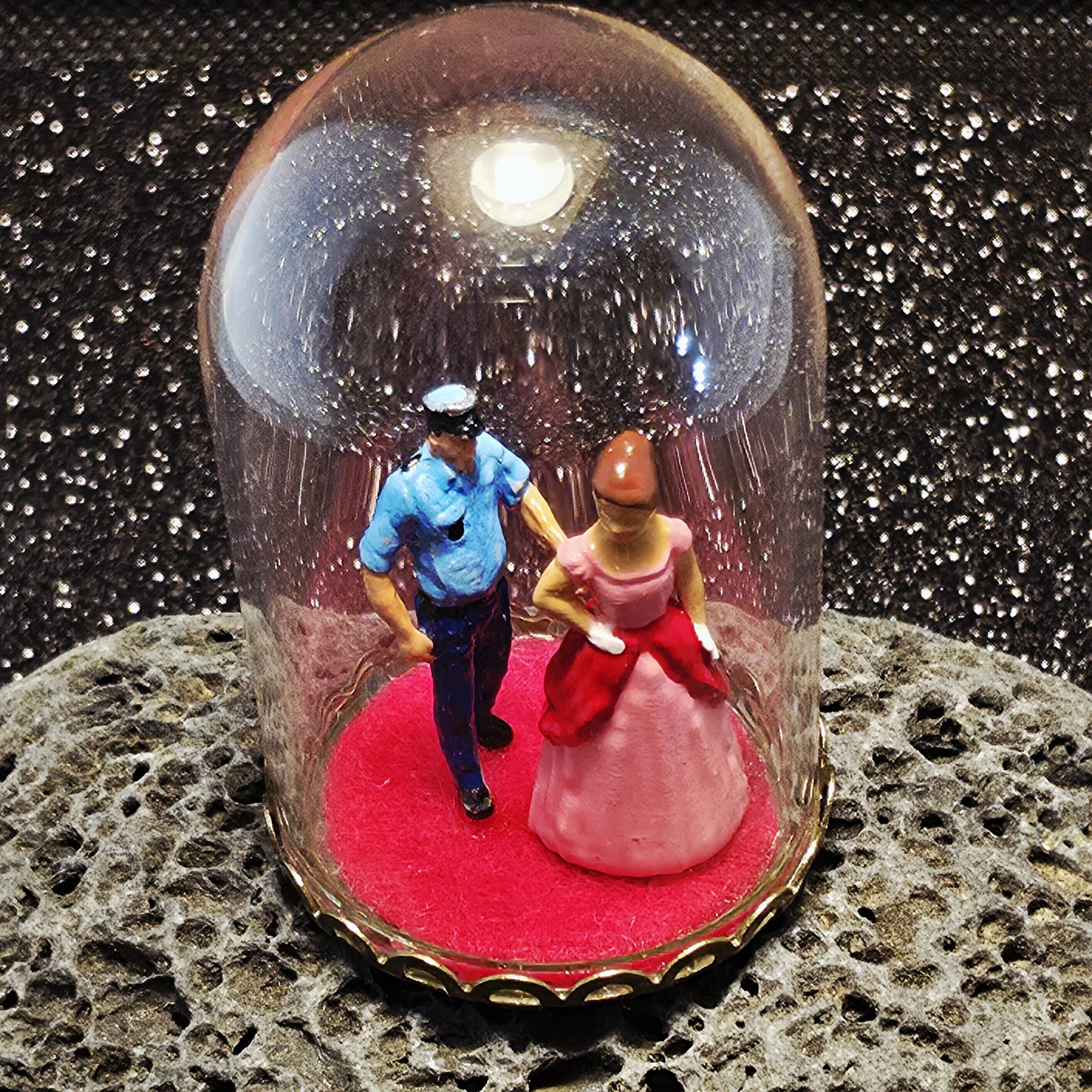 une bulle de verre exposant un policier tenant par le bras une princesse en robe rose.