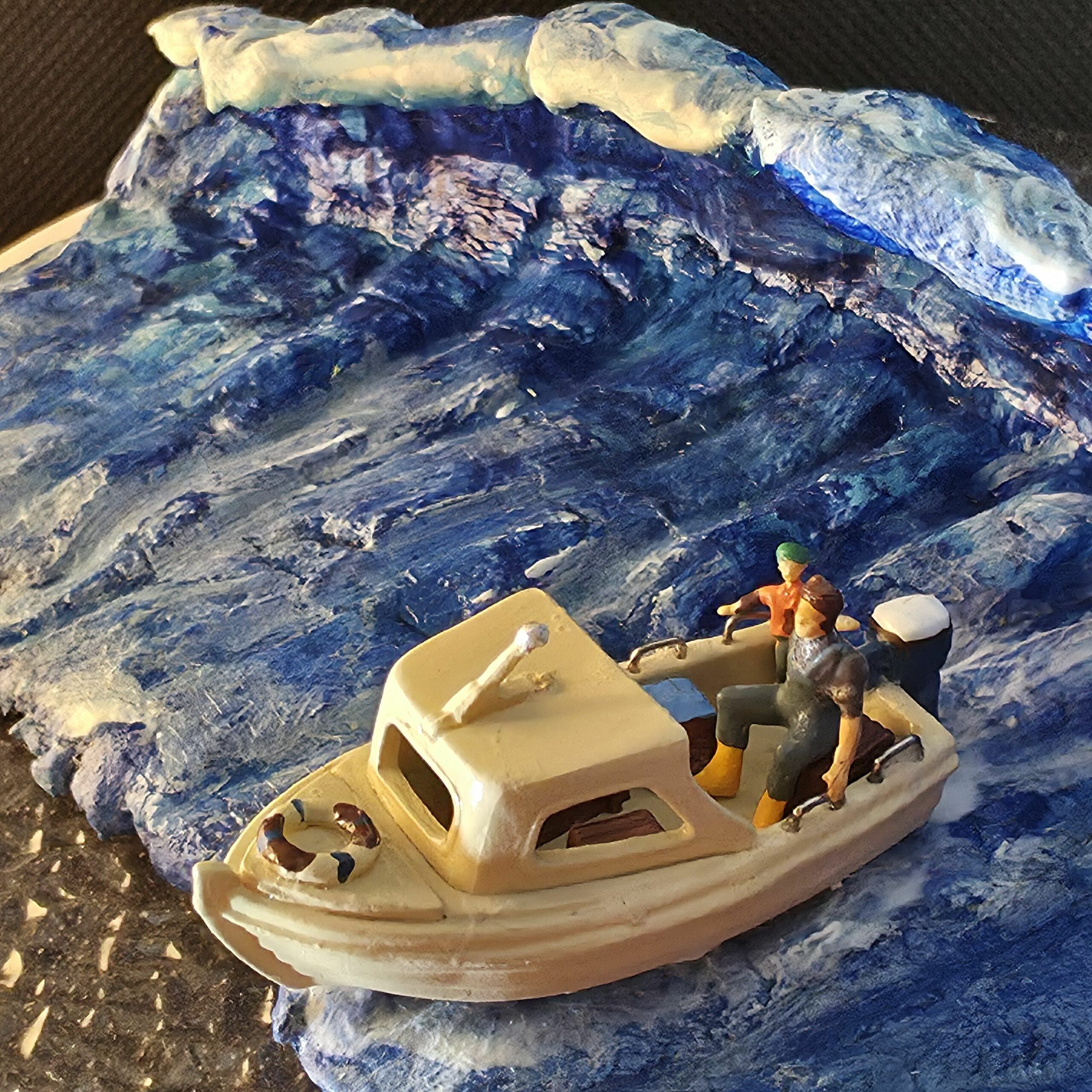 Sculpture en argile peinte représentant une vague tsunami ou raz-de-marée déferlante qu'essaie de fuir un petit bateau à moteur