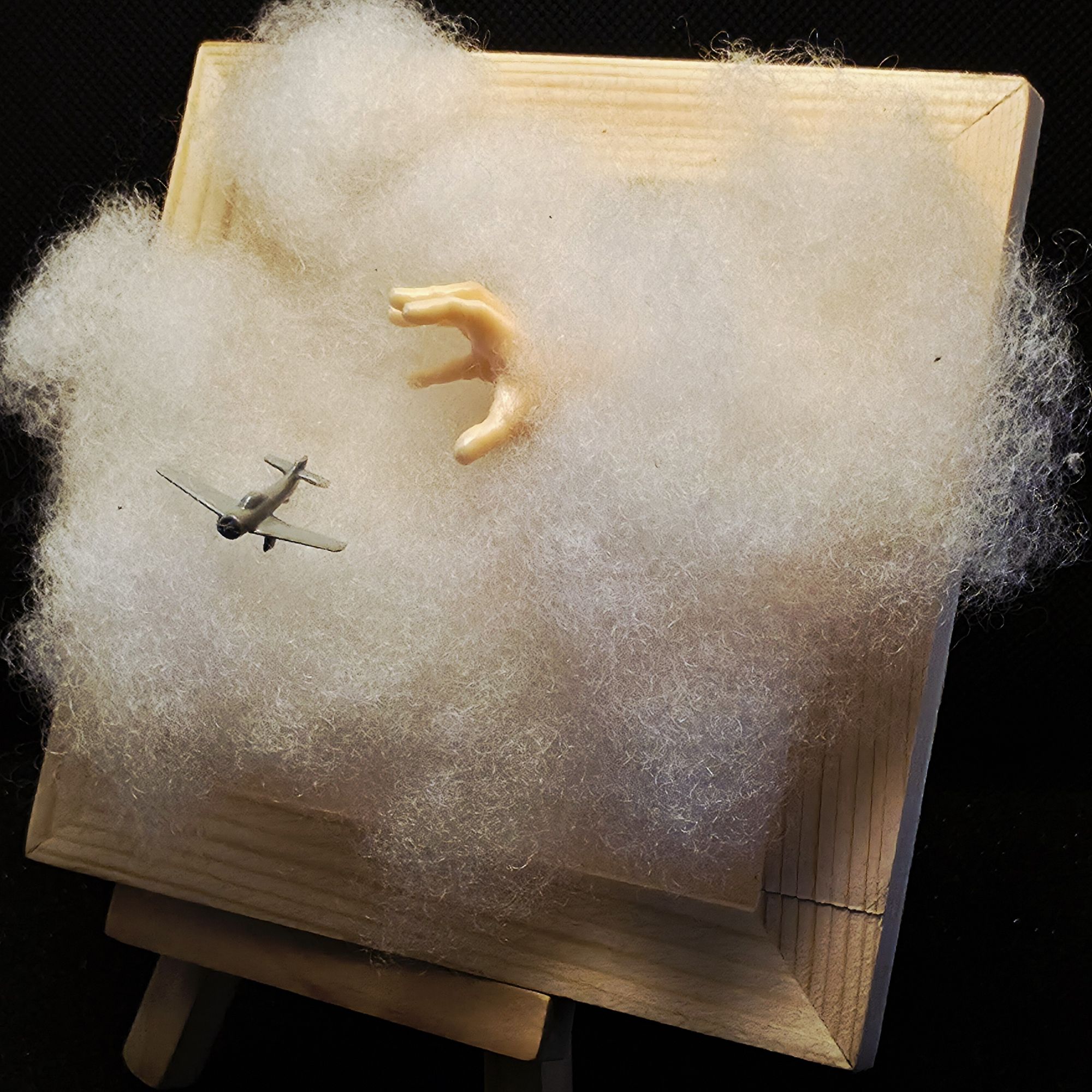 Petit tableau figurant un avion en perdition dans un nuage qu'essaie d'attraper une main géante qui surgit du nuage